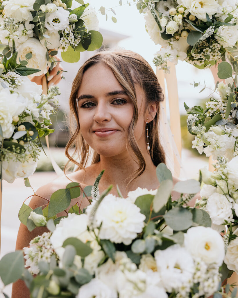 Bride soft smiles with bouquets framing her face
