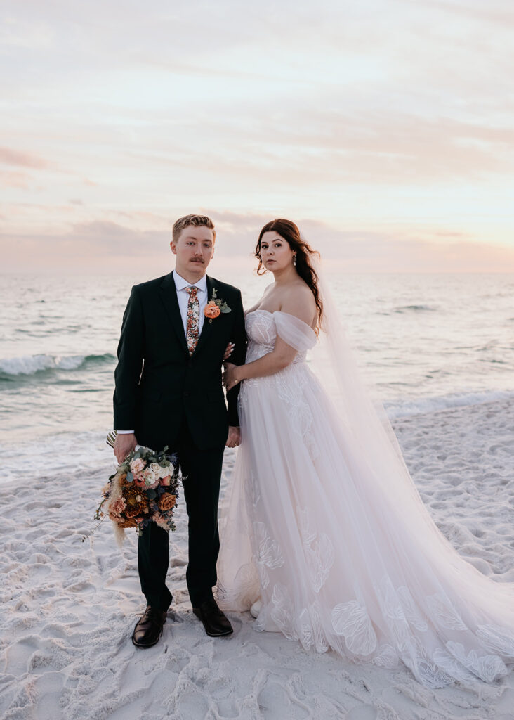 bride and groom stand by the ocean