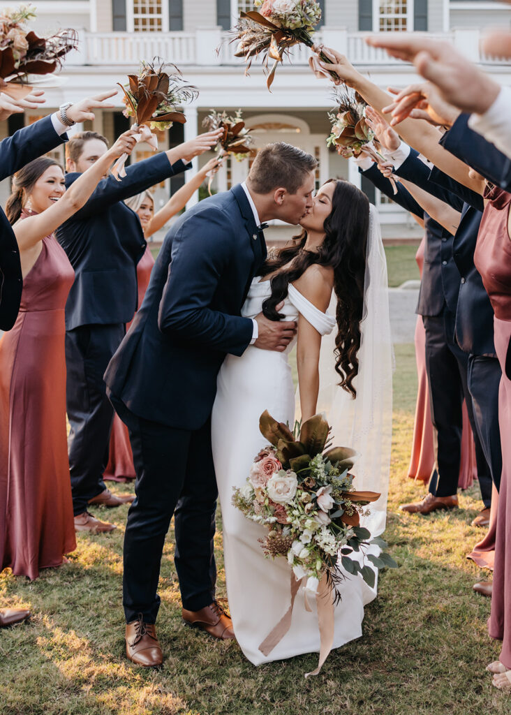 bride and groom kiss while wedding party cheers