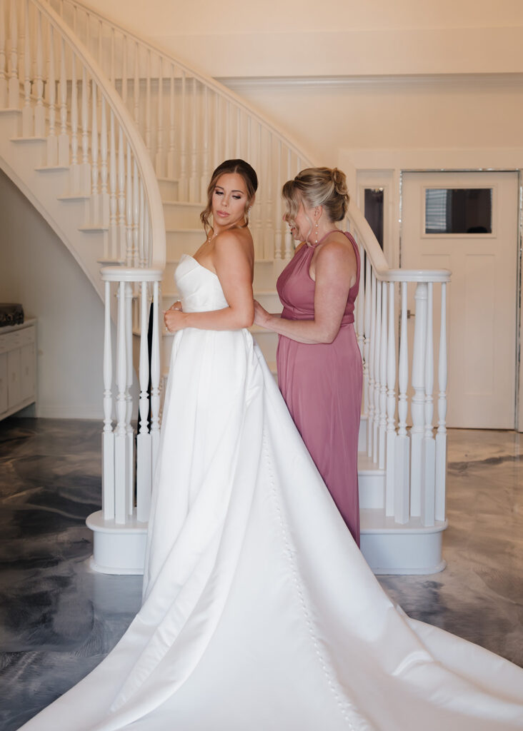 mother of the bride helps the bride into her wedding dress