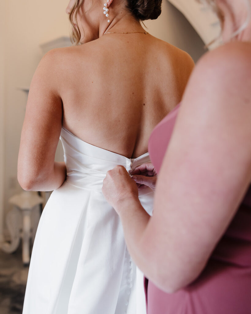 mother of the bride helps the bride into her wedding dress