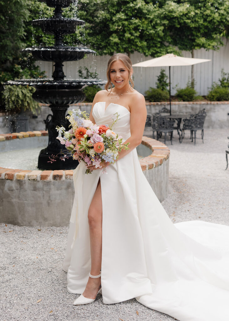 bride holds her bouquet in front of Supposey's fountain
