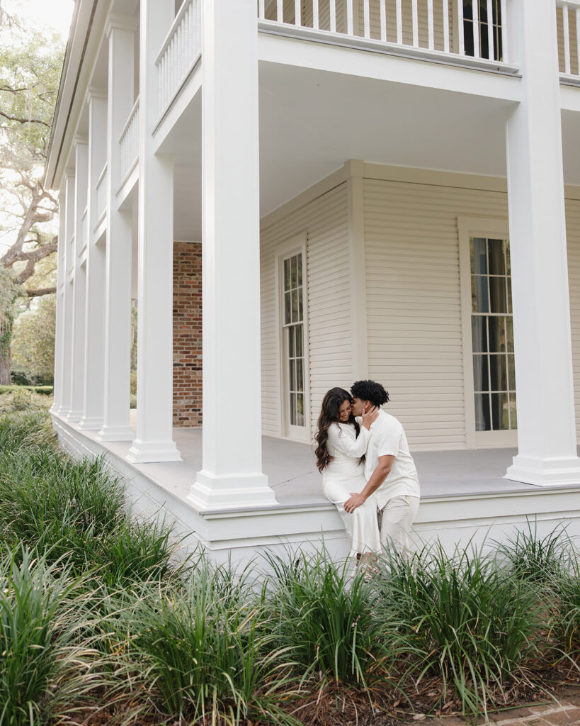 man kisses woman's cheek as they sit by the Wesley mansion at Eden Gardens State Park