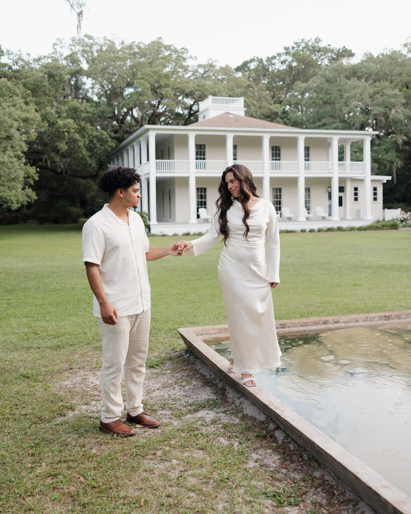 woman balances on a fountain while man leads her at Eden Gardens State Park