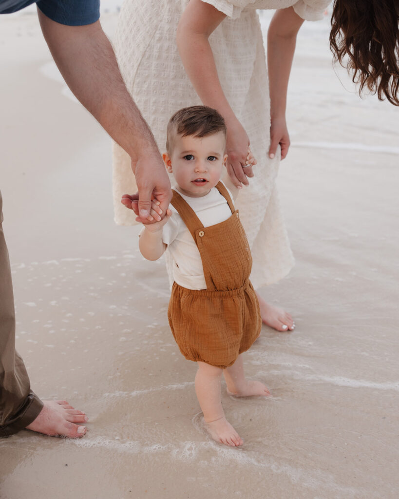 baby sticks his feet in the ocean