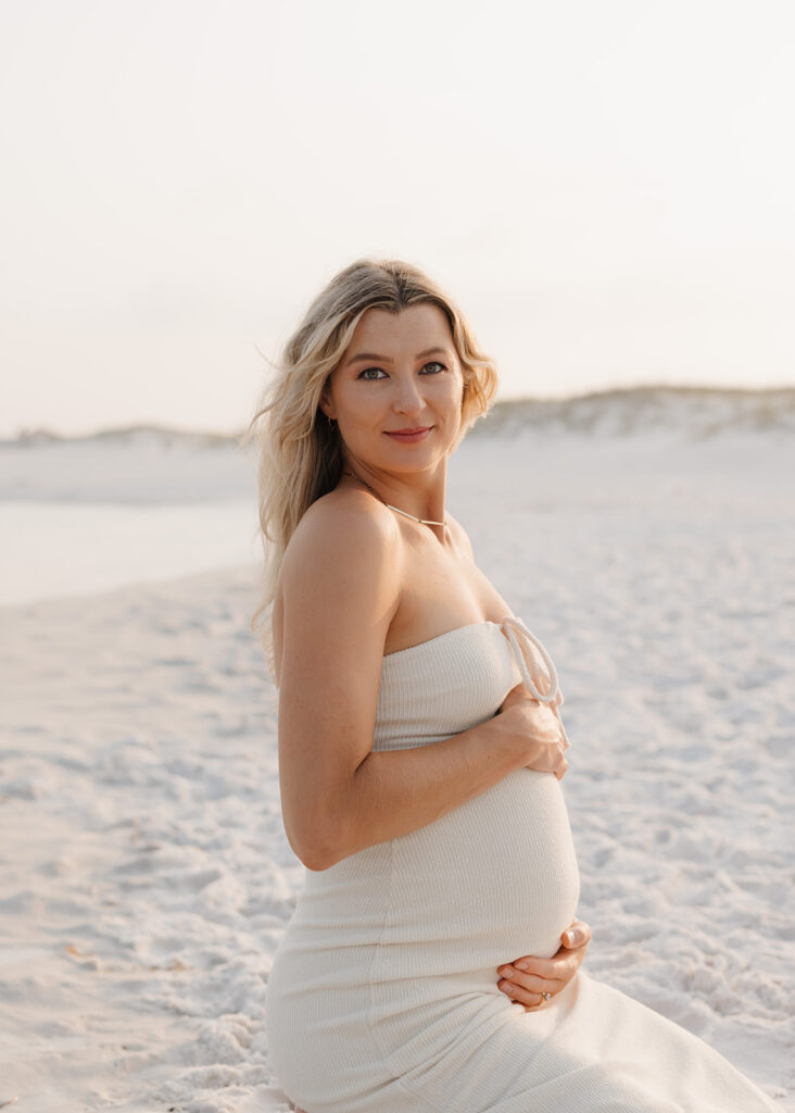 woman holds her pregnant stomach on Destin, Florida beach