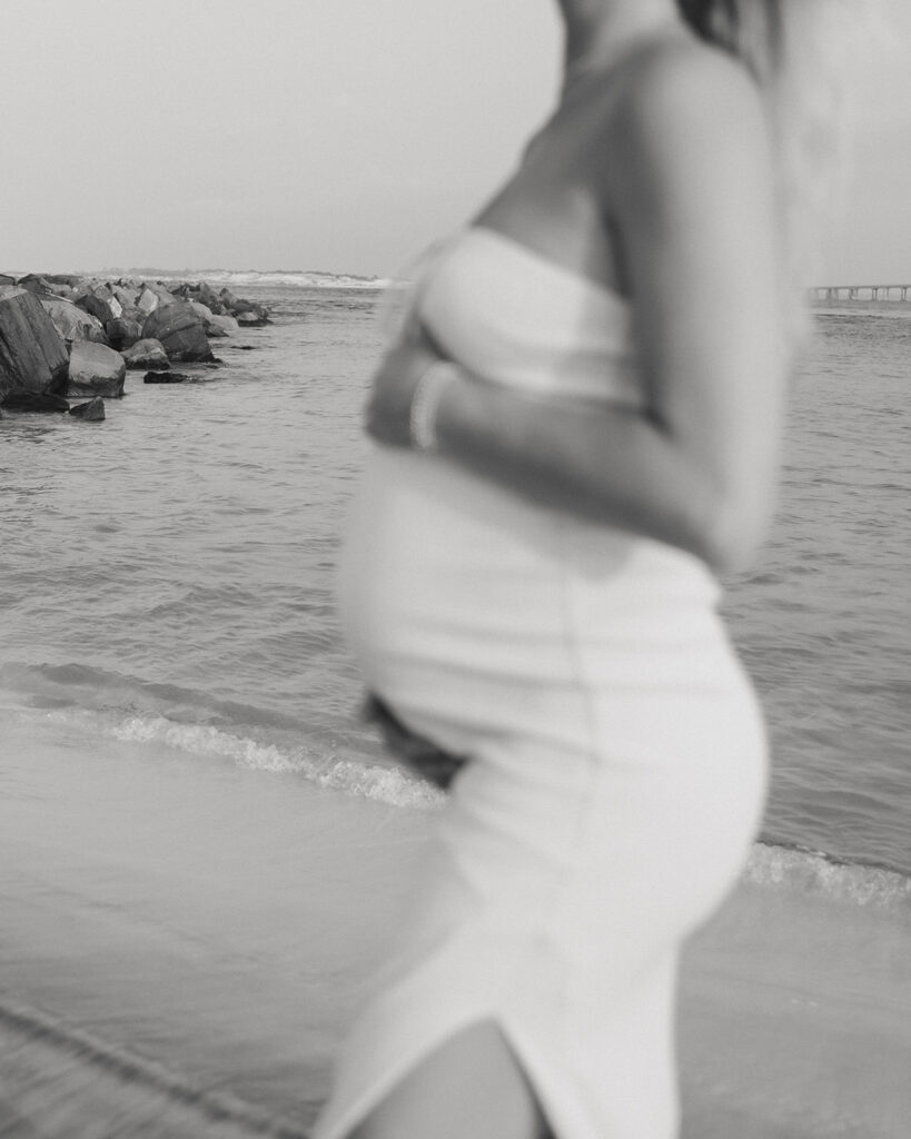 woman holds her pregnant stomach on Destin, Florida beach