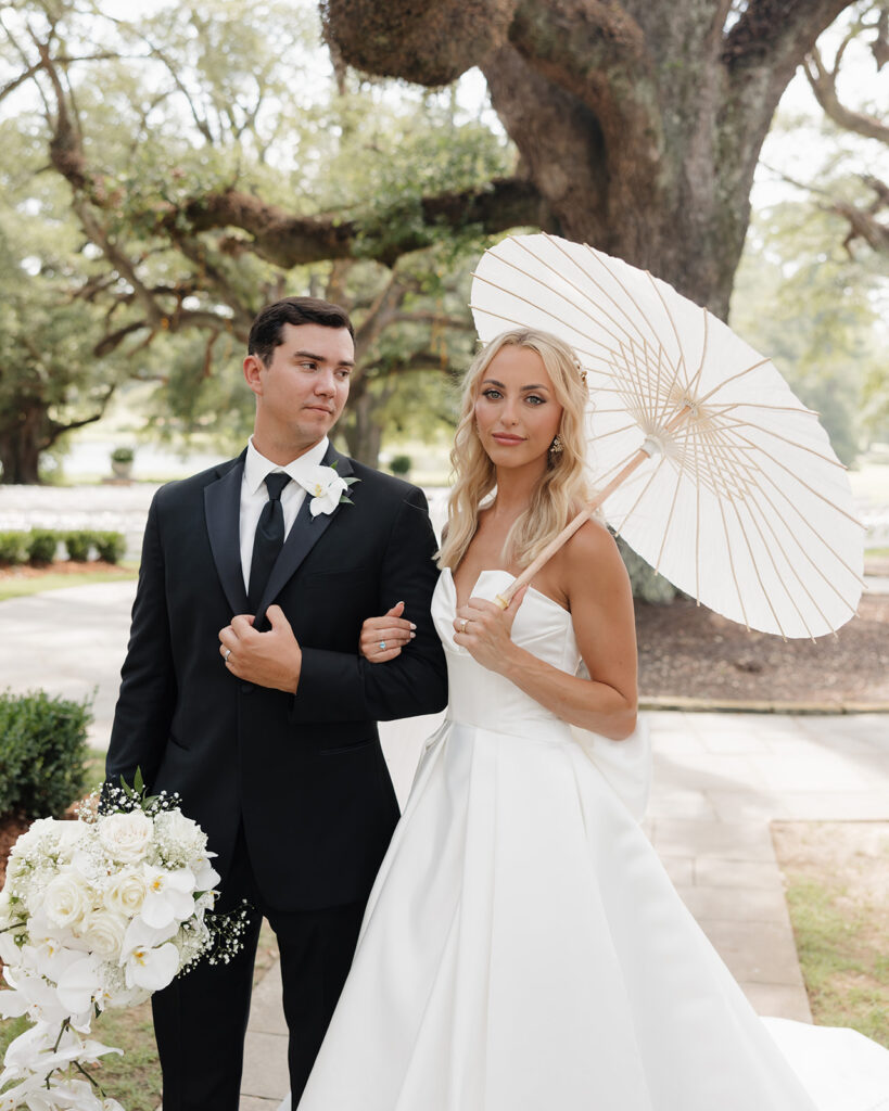 bride holds a parasol as her groom smiles at her