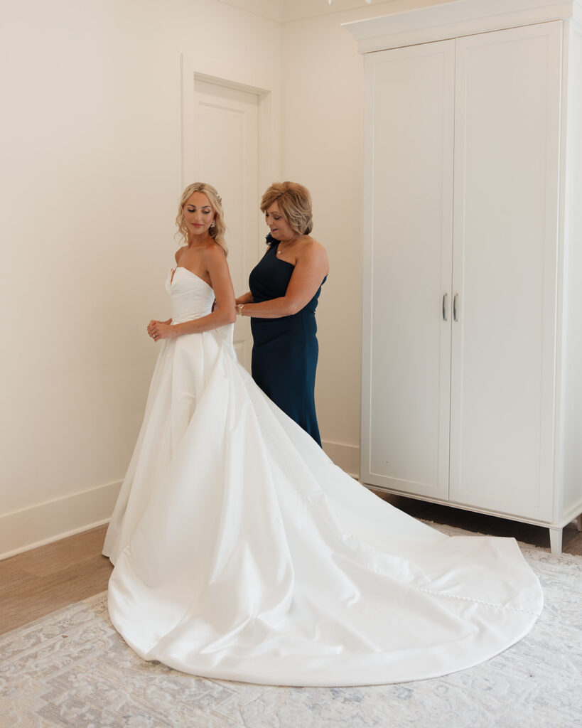 bride's mother zips up the bride's wedding dress