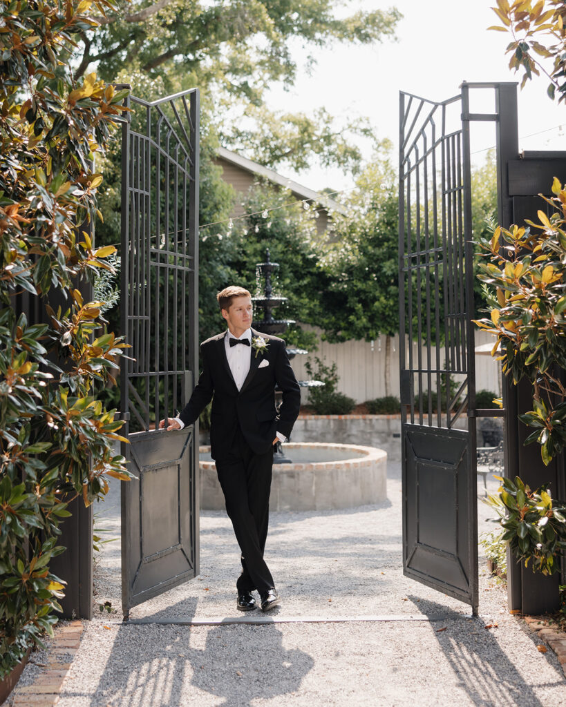 groom poses in the middle of an open gate