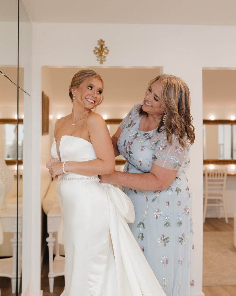 mother of the bride helps bride into her wedding dress