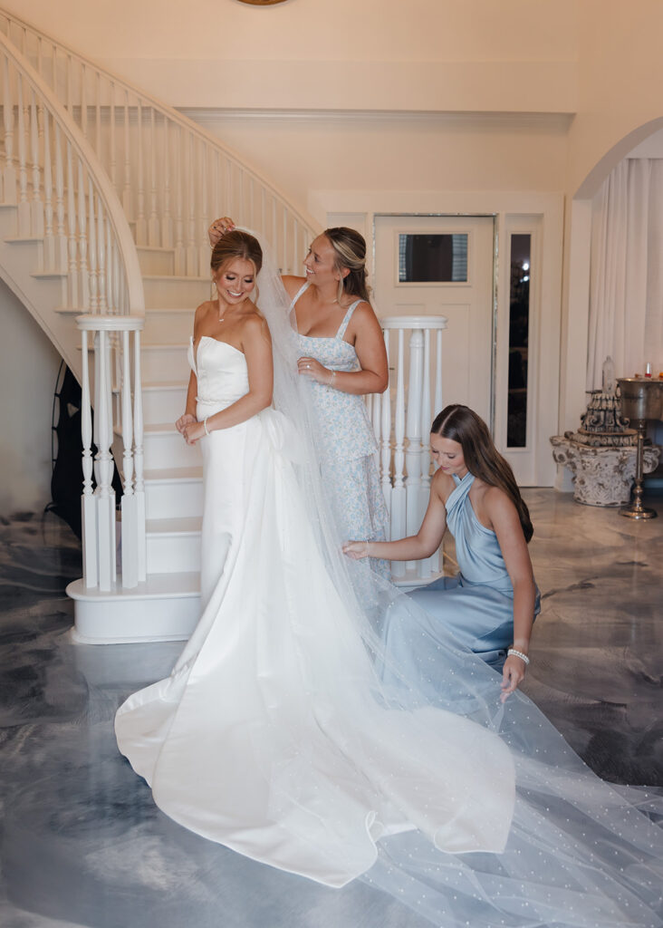 sisters of the bride adjust the bride's dress and veil