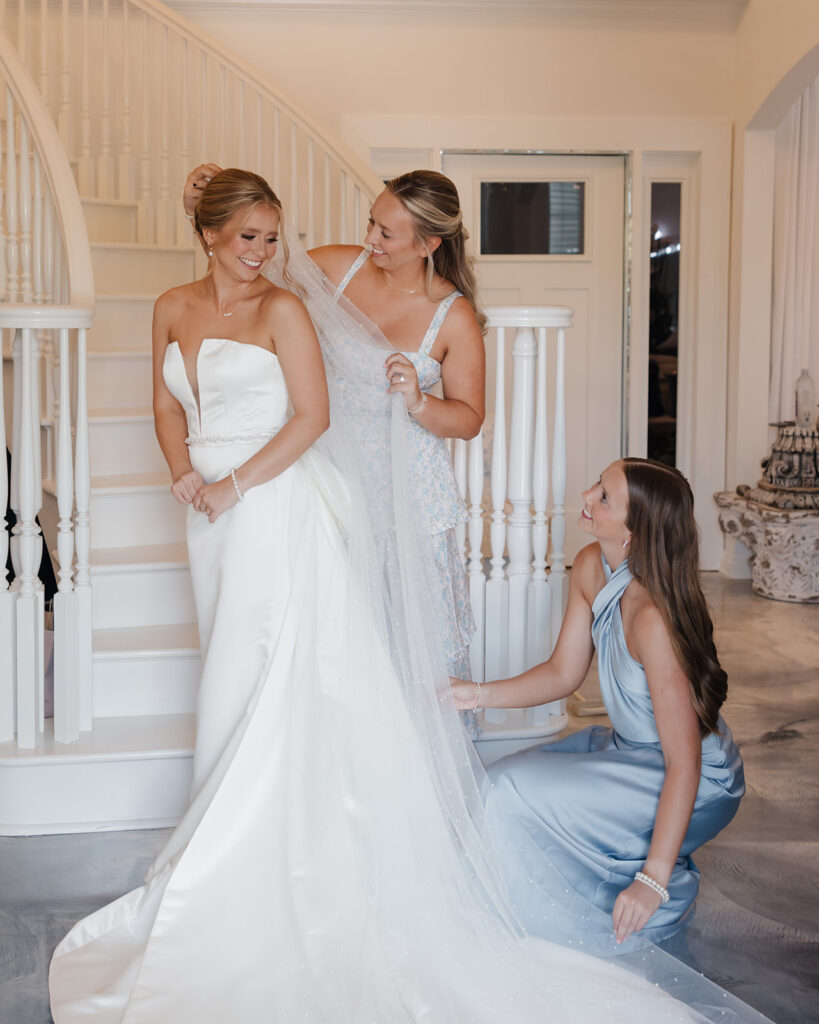 sisters of the bride adjust the bride's dress and veil