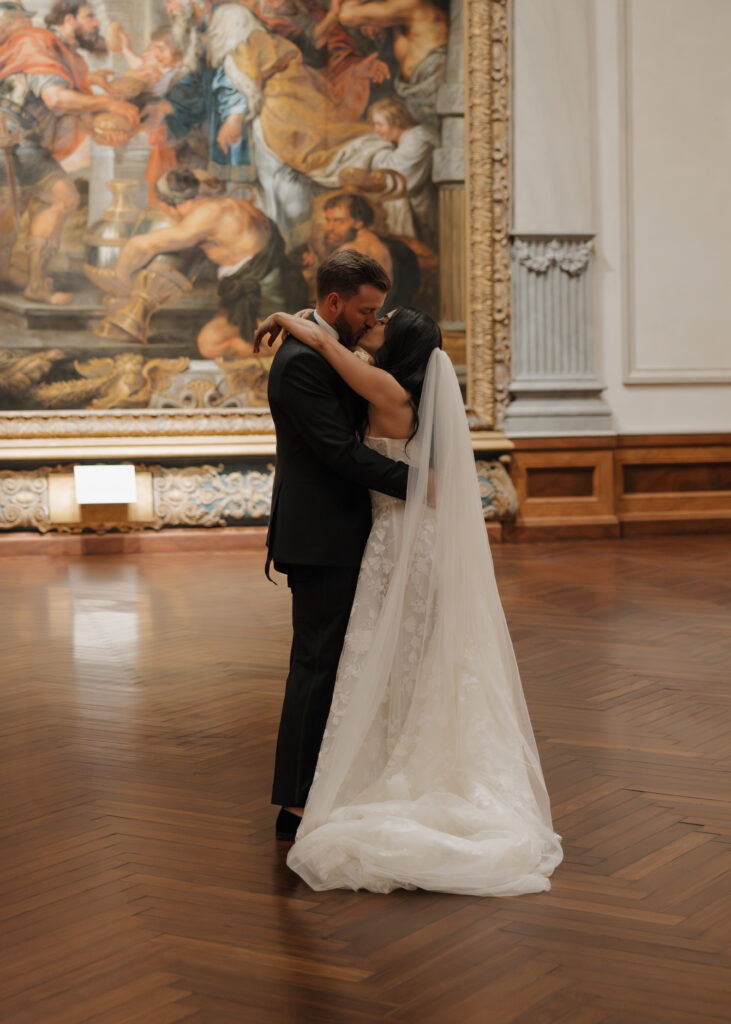 bride and groom kiss in front of a painting