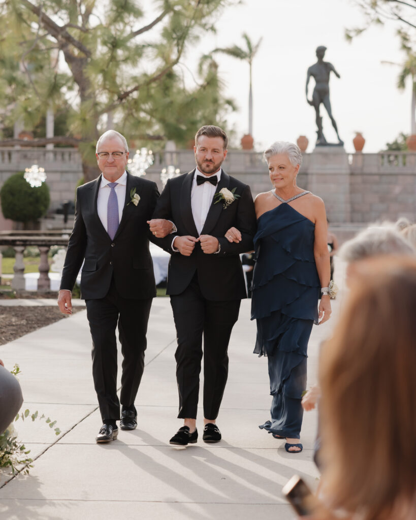 groom escorts his parents down the aisle