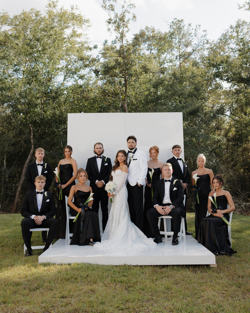 The wedding party poses by a white backdrop