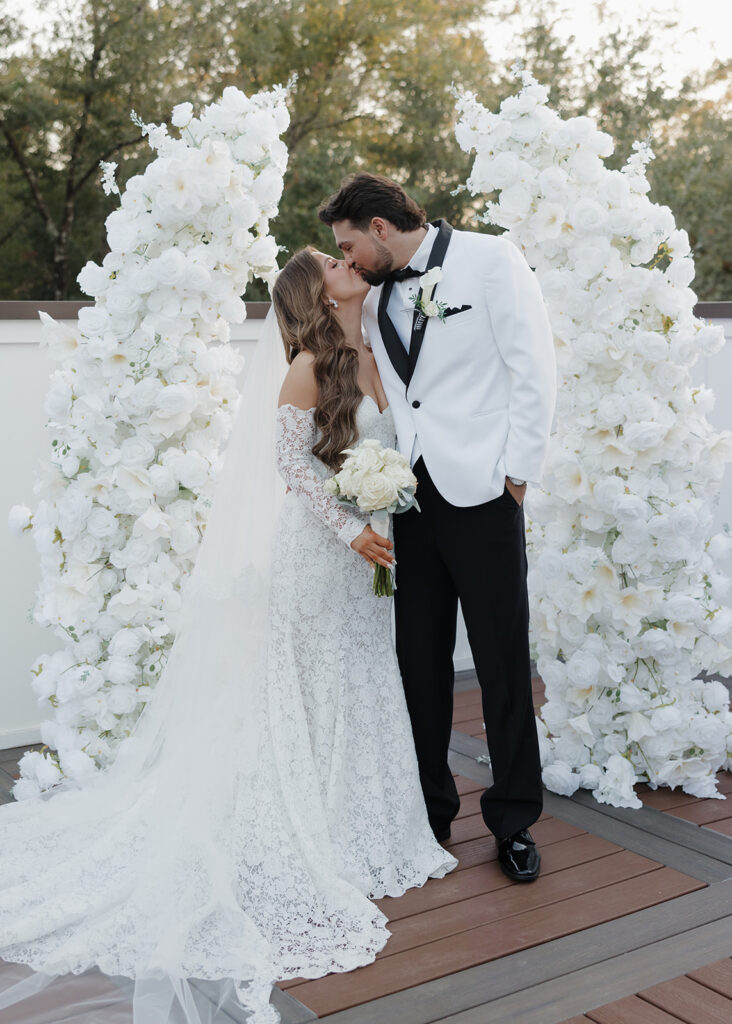 bride and groom kiss by large floral arch